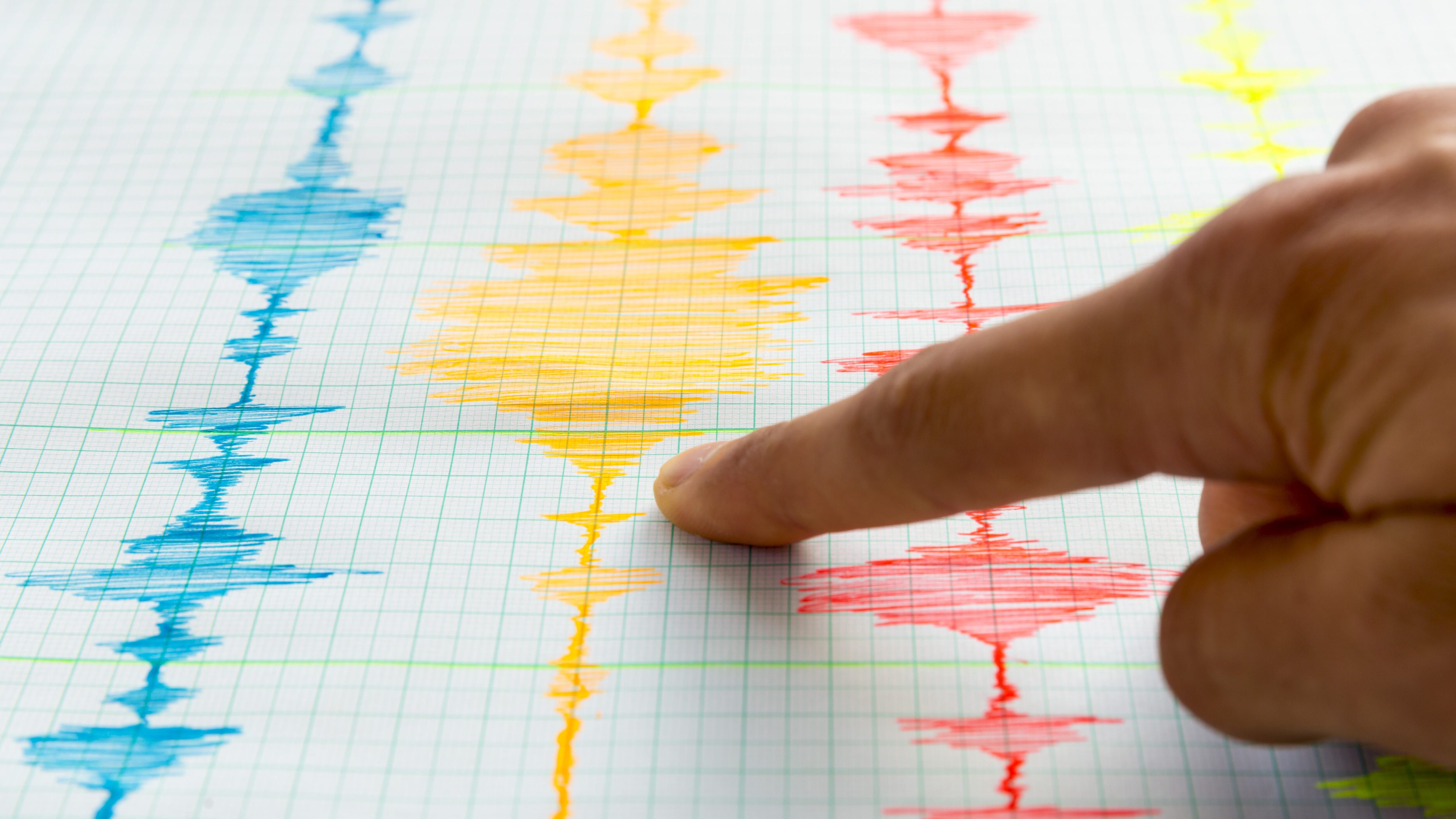Seismological device for measuring earthquakes. Seismological activity live on the sheet of measuring paper. Earthquake wave on graph paper. Human hand showing earthquake.