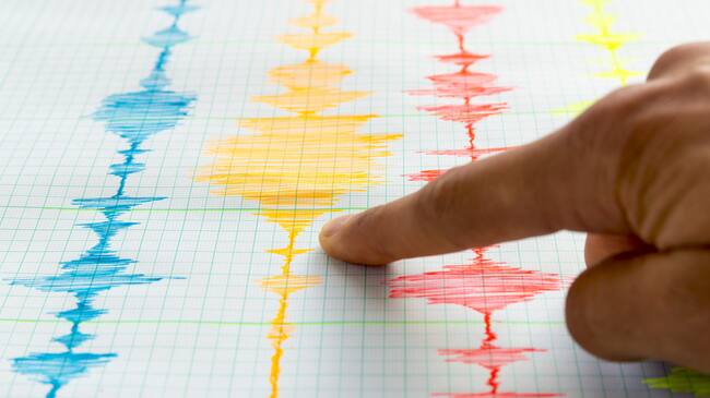 Seismological device for measuring earthquakes. Seismological activity live on the sheet of measuring paper. Earthquake wave on graph paper. Human hand showing earthquake.