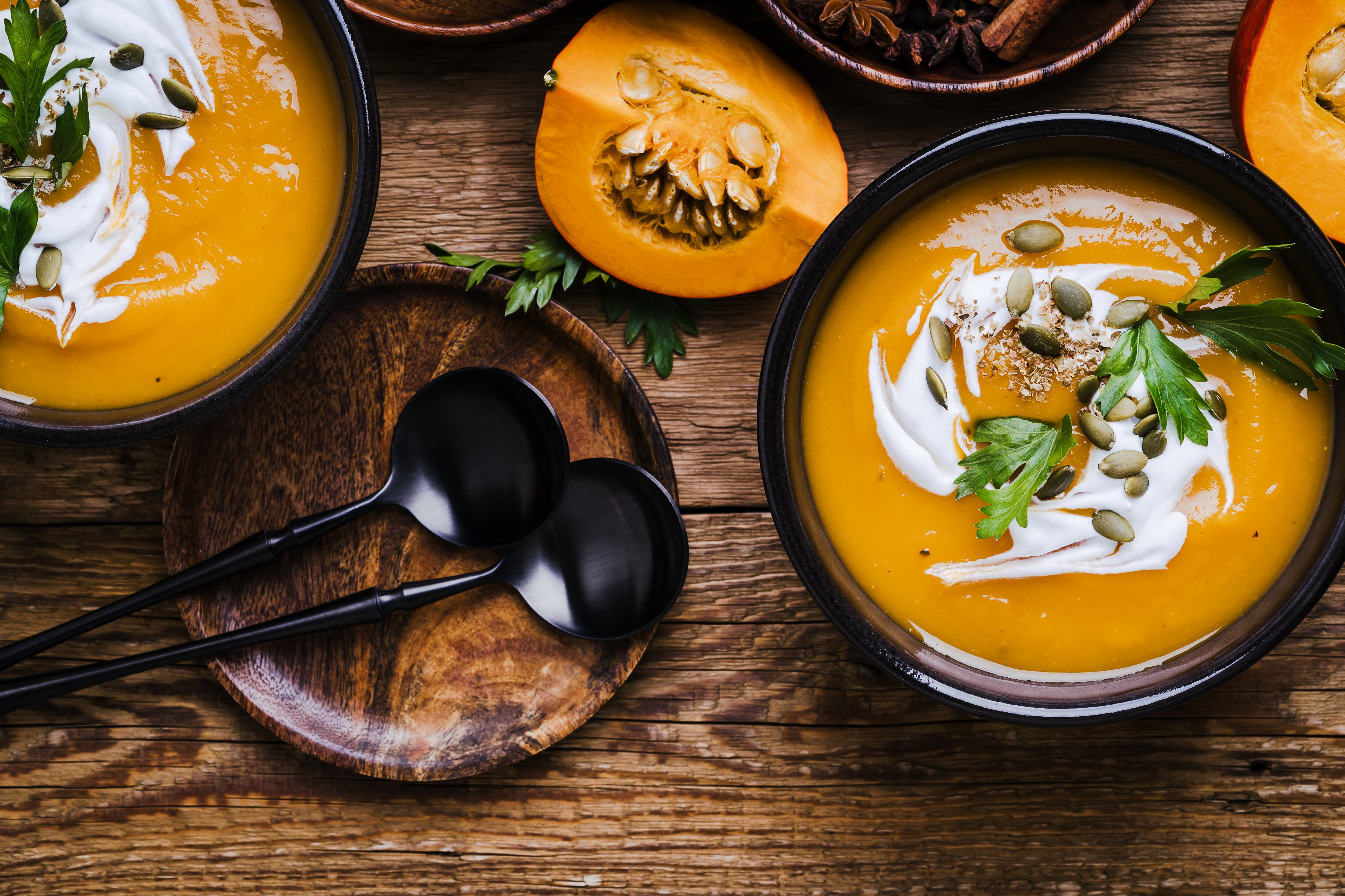 Pumpkin soup in ceramic bowl, traditional autumn comfort food, Thanksgiving favorite meal on wooden rustic table viewed from above