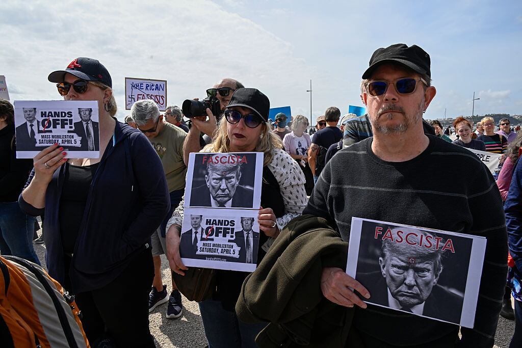 LISBON, PORTUGAL - APRIL 05: US residents in Portugal hold placards while gathering in Praça do Comercio during a protest organized by American activists living in Portugal, with the common goal of fighting against the political plans of Trump and Elon Musk, and against “the destruction of democratic institutions” in the United States on April 05, 2025, in Lisbon, Portugal. The actions are part of the #HandsOff Day of Action and Solidarity, the demonstration “Lisbon against attacks! Hands off!” in protest against US President Donald Trump and Elon Musk. (Photo by Horacio Villalobos#Corbis/Corbis via Getty Images)