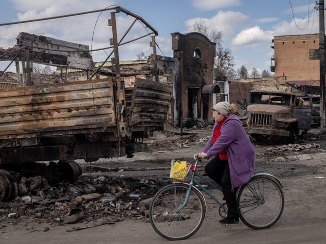 Mujer en bicicleta pasa ante vehículos destruidos por ataques en Trostyanets
