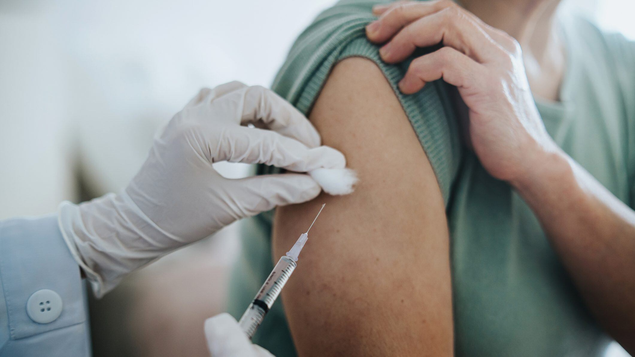 Close up of senior Asian woman getting Covid-19 vaccine in arm for Coronavirus immunization by a doctor at hospital. Elderly healthcare and illness prevention concept