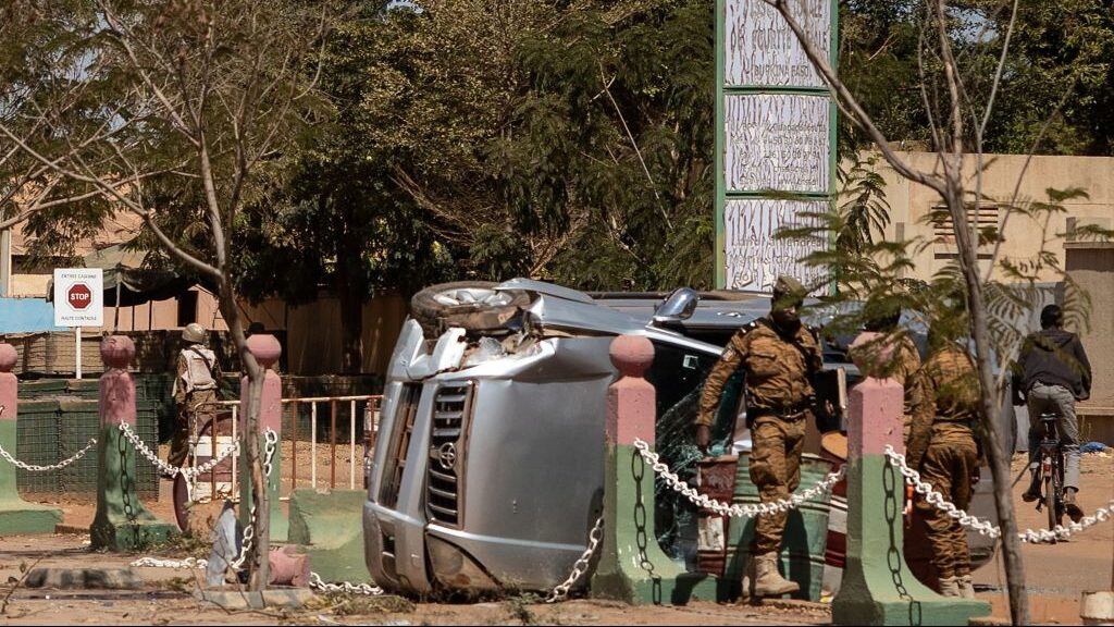 Burkina Faso soldiers stand by a damaged vehicle in front of the Guillaume Ouedraogo military camp in Ouagadougou on January 24, 2022. - Mutinous troops in Burkina Faso arrested and detained President Roch Marc Christian Kabore and his ministers on January 24, 2022, demanding more resources for the battle against Islamist insurgents, security sources told AFP.The arrests came a day after soldiers at several barracks across the volatile West African country staged an uprising over the government's handling of the jihadist threat. (Photo by OLYMPIA DE MAISMONT / AFP) (Photo by OLYMPIA DE MAISMONT/AFP via Getty Images)