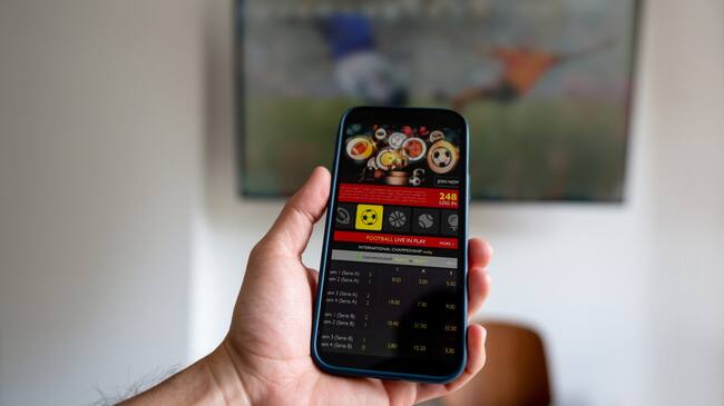Man watching a football match and gambling on a mobile app - sports betting concepts. **DESIGN ON BOTH SCREENS WERE MADE FROM SCRATCH BY US**