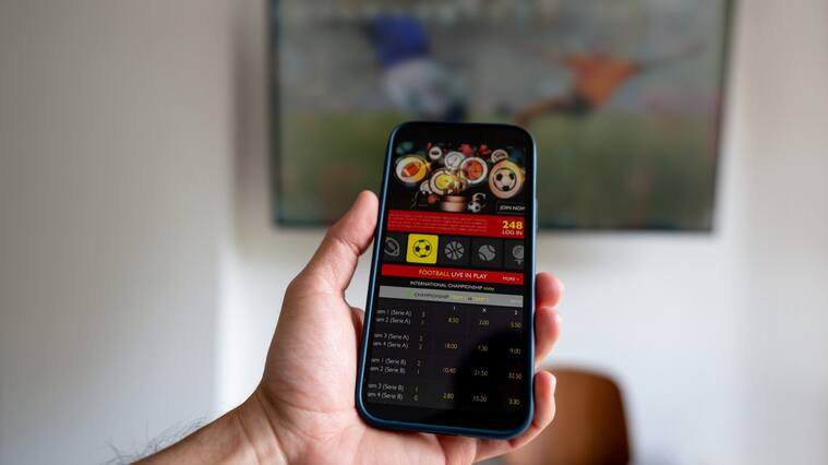 Man watching a football match and gambling on a mobile app - sports betting concepts. **DESIGN ON BOTH SCREENS WERE MADE FROM SCRATCH BY US**