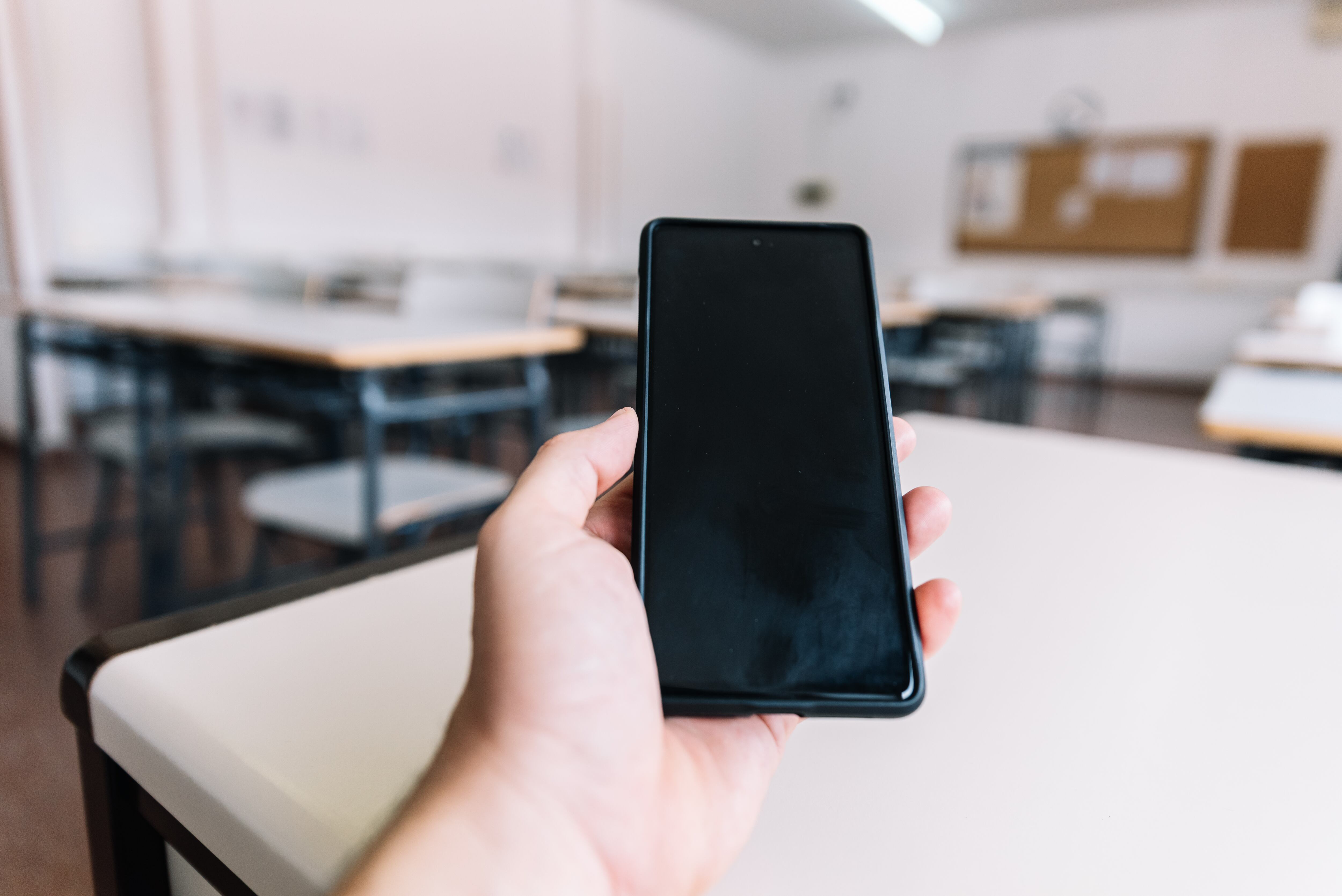 Hand holding a cell phone in a classroom at school