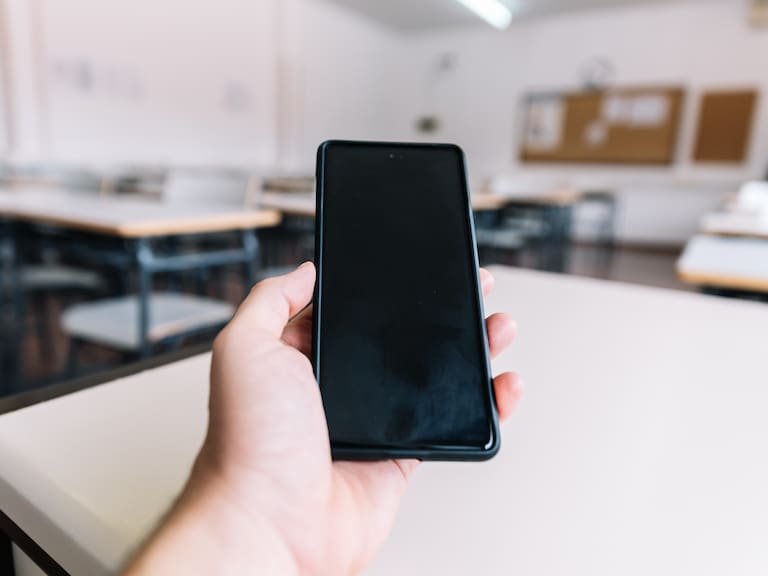 Hand holding a cell phone in a classroom at school