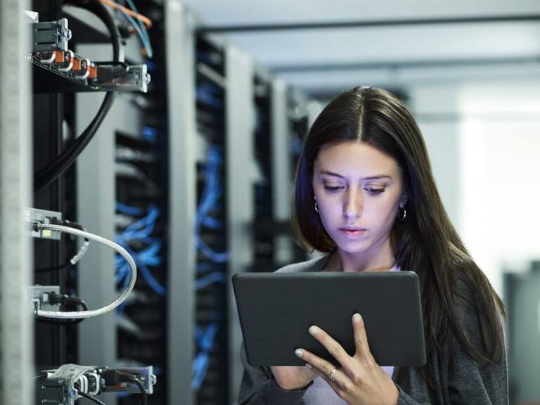 Female technician using digital tablet in server room. IT professional is standing at workplace. She is in casuals.