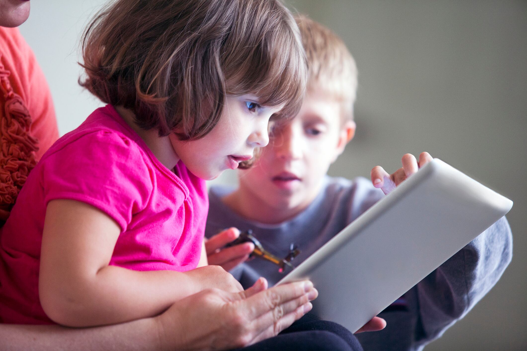 A mother looking at a tablet device with her son and daughter inside their home.
