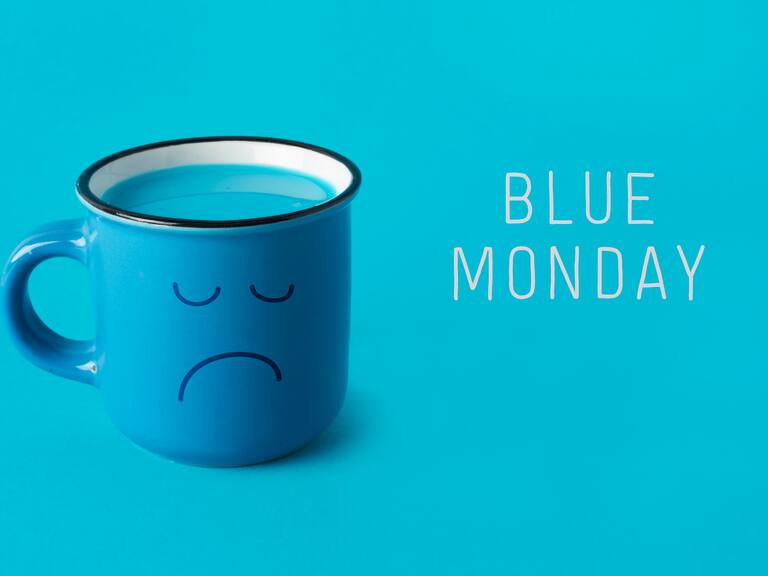 closeup of a blue mug, with a sad face drawn in it, and the text blue monday on a blue background