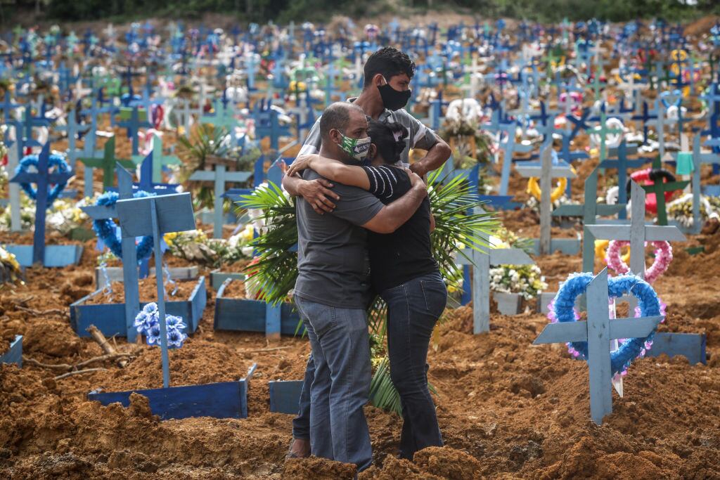 Familiares de una víctima del covid-19 lloran en un cementerio de Brasil