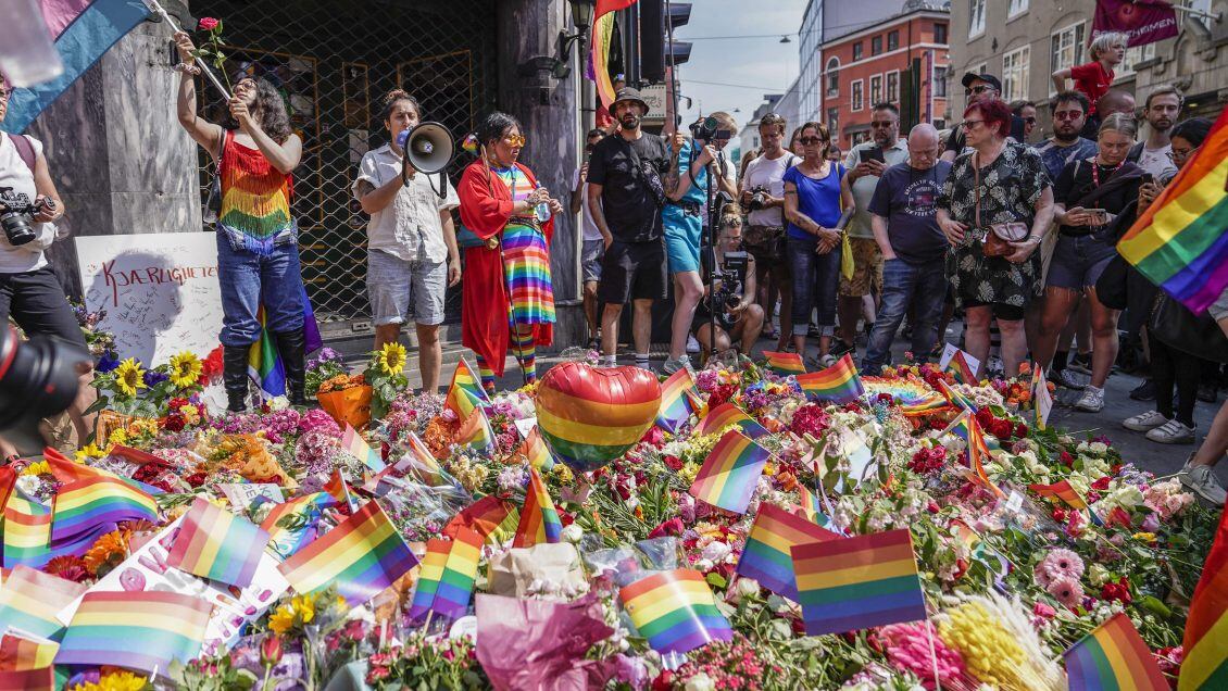 People with Pride flags stand near the London pub and lay flowers on June 25, 2022, in the aftermath of a shooting outside pubs and nightclubs in central Oslo killing two people injuring 21. - The Pride march that was due to take place in Norway's capital Oslo on Saturday afternoon has been called off after deadly overnight shootings, including near a gay bar, organisers said. - Norway OUT (Photo by Håkon Mosvold Larsen / NTB / AFP) / Norway OUT (Photo by HAKON MOSVOLD LARSEN/NTB/AFP via Getty Images)