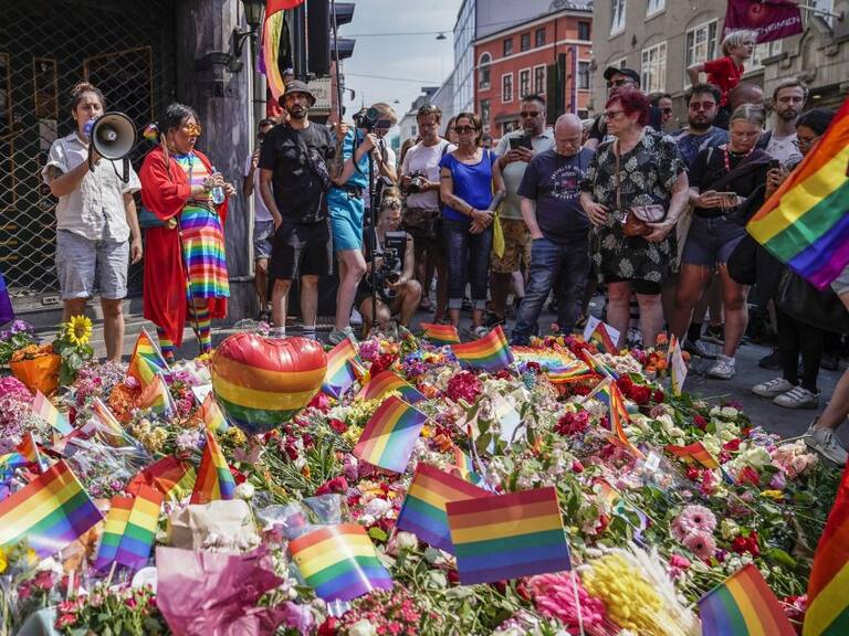 People with Pride flags stand near the London pub and lay flowers on June 25, 2022, in the aftermath of a shooting outside pubs and nightclubs in central Oslo killing two people injuring 21. - The Pride march that was due to take place in Norway's capital Oslo on Saturday afternoon has been called off after deadly overnight shootings, including near a gay bar, organisers said. - Norway OUT (Photo by Håkon Mosvold Larsen / NTB / AFP) / Norway OUT (Photo by HAKON MOSVOLD LARSEN/NTB/AFP via Getty Images)