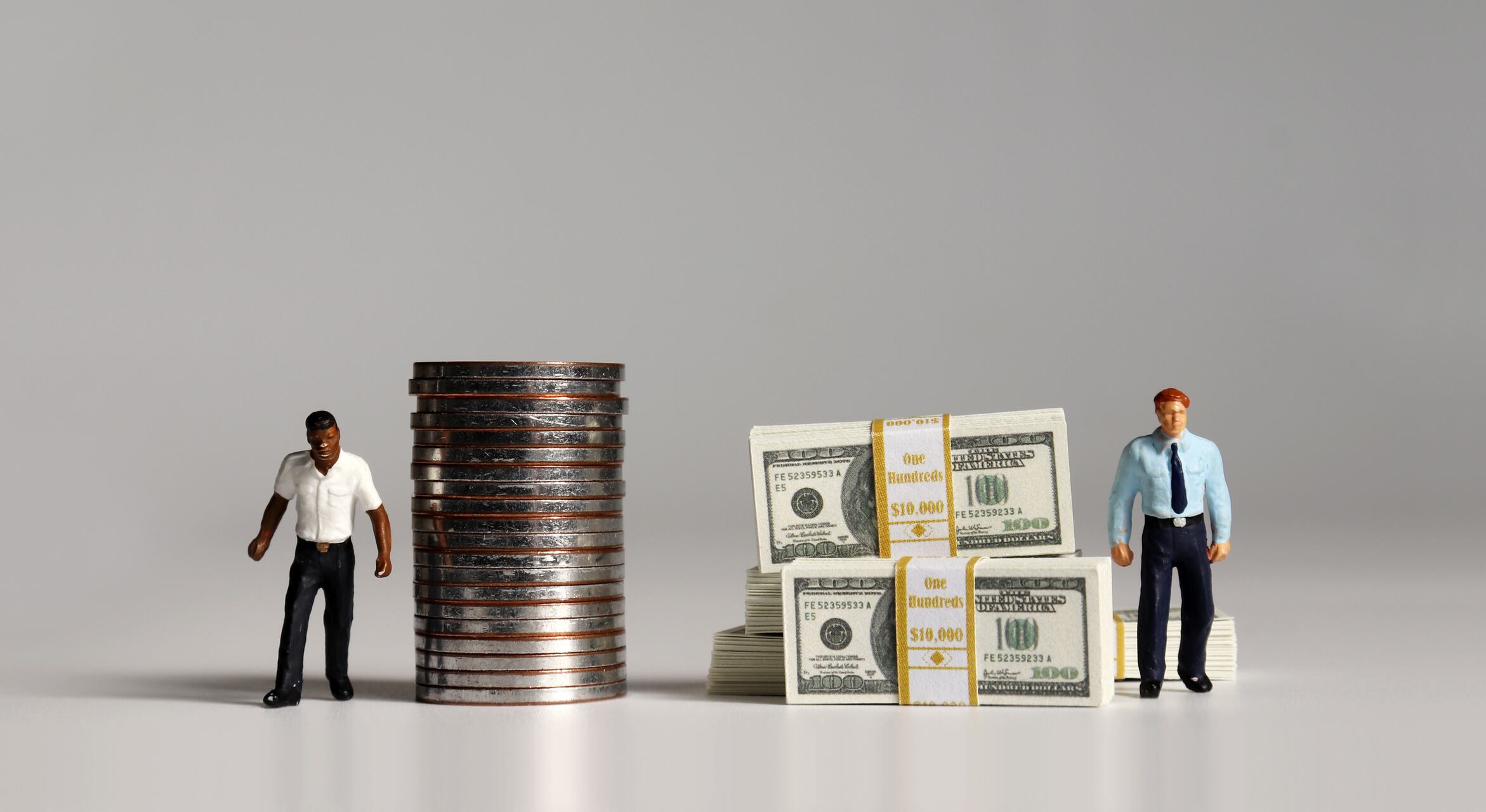 A pile of bills and coins. Miniature people. The concept of racial and income disparity.