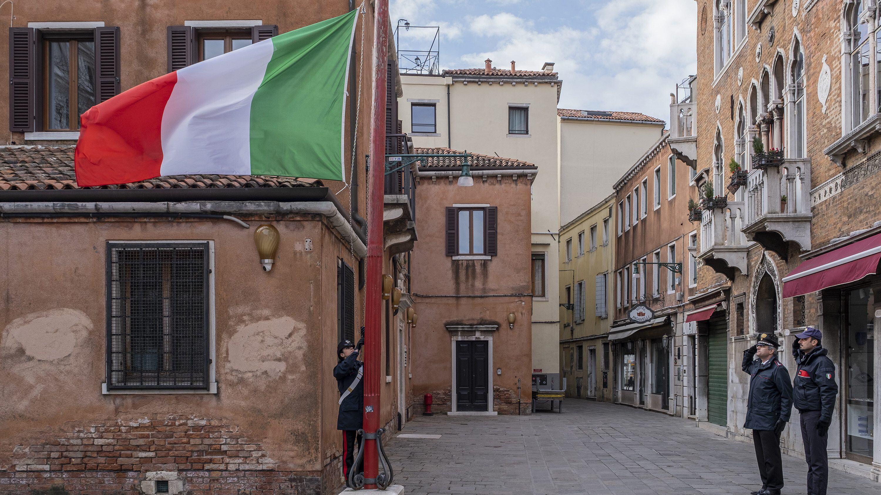 VENICE, ITALY - MARCH 31: Carabinieri raise the flag at half-mast to remember people dying of corona virus on March 31, 2020 in Venice, Italy. The Italian government continues to enforce the nationwide lockdown measures to control the spread of COVID-19. (Photo by Stefano Mazzola/Awakening/Getty Images)