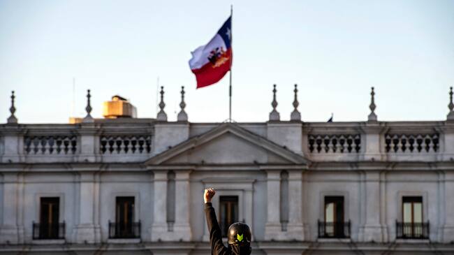 TOPSHOT - A demonstrator raises his clenched fist in front of La Moneda presidential palace during a protest against Chilean President Sebastian Pinera's government in Santiago, on December 20, 2019. - Pinera promised support for victims of human rights violations by security forces during protests in Chile, and a firm commitment to achieve truth and justice. (Photo by Martin BERNETTI / AFP) (Photo by MARTIN BERNETTI/AFP via Getty Images)