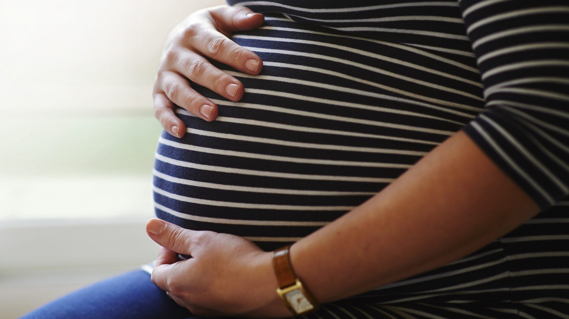 Heavily pregnant female sitting by window, holding her bump with both hands.