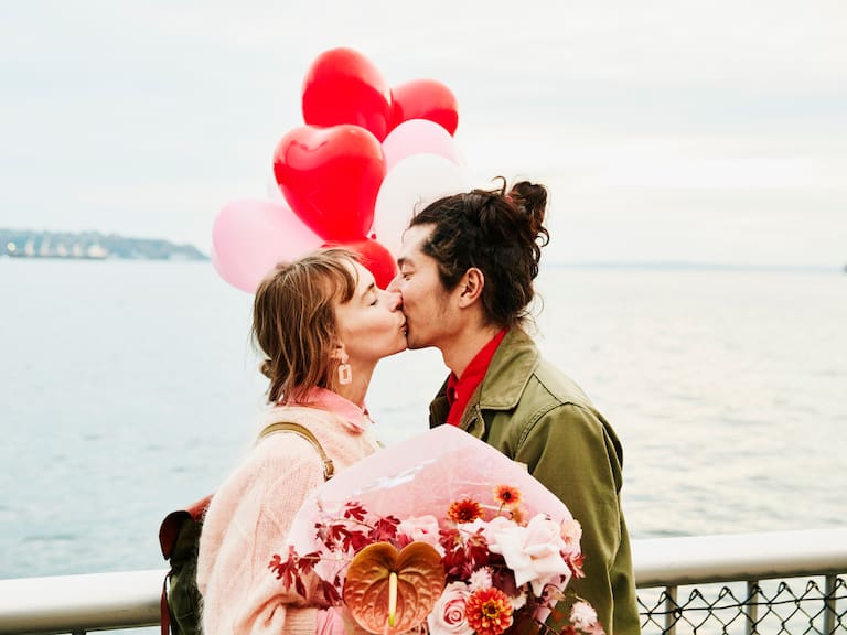 Couple holding heart shaped balloons kissing while exploring city