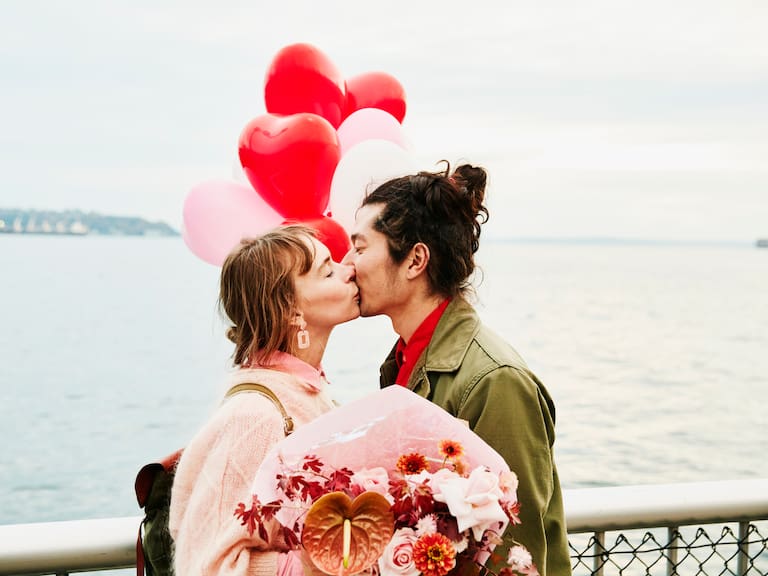Couple holding heart shaped balloons kissing while exploring city