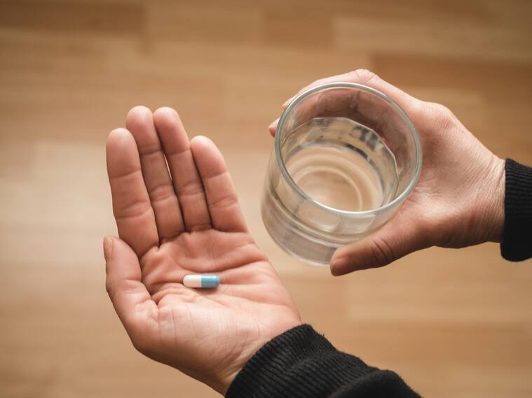 A woman's hand holding a pill with a wood floor as background