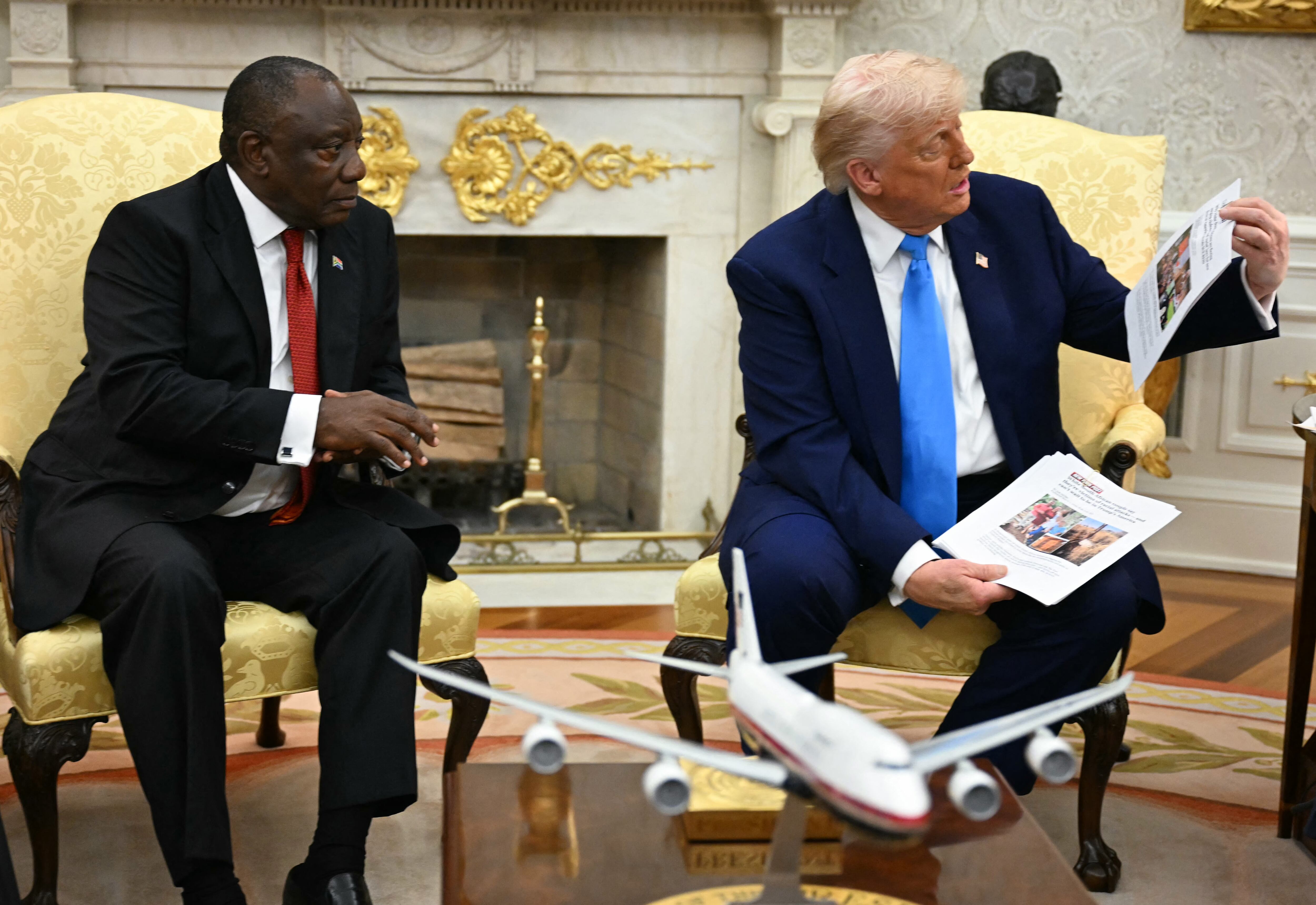 US President Donald Trump shows pictures and articles as he meets with South African President Cyril Ramaphosa in the Oval Office of the White House in Washington, DC, on May 21, 2025. South African President Cyril Ramaphosa meets Donald Trump on Wednesday amid tensions over Washington's resettlement of white Afrikaners that the US president claims are the victims of "genocide." (Photo by Jim WATSON / AFP) (Photo by JIM WATSON/AFP via Getty Images)