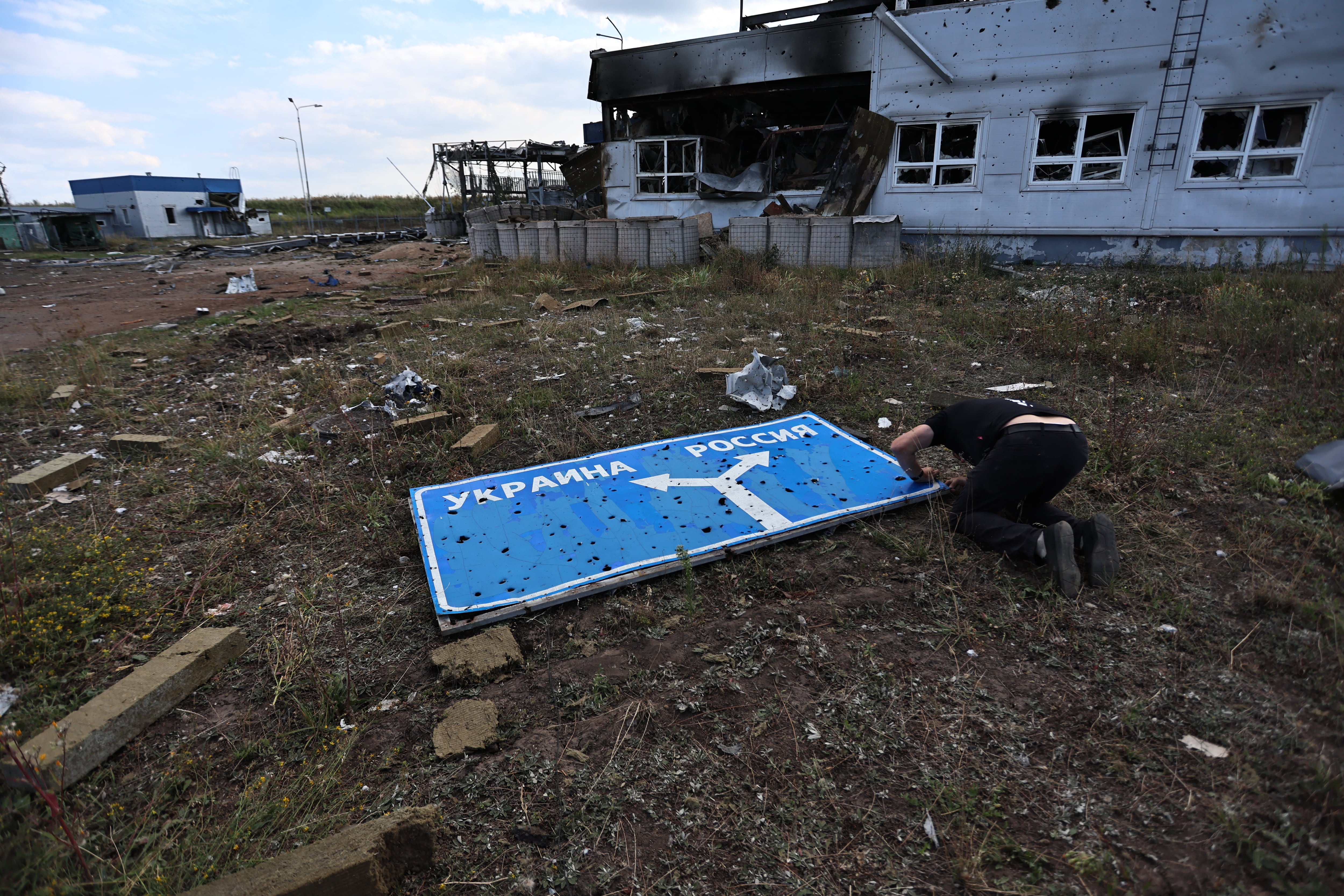 TOPSHOT - This photograph taken on 16 August, 2024, during a media tour organised by Ukraine, shows a man examining a damaged road sign with directions to Ukraine and Russia at a destroyed border crossing point near the Ukrainian-controlled Russian town of Sudzha, Kursk region, amid the Russian invasion in Ukraine. Kyiv said August 16, 2024, its incursion into Russian territory had advanced, claiming it aimed to force Russia to negotiate on "fair" terms, as Moscow's troops announced new gains in eastern Ukraine. Two and a half years into Russia's invasion of Ukraine, Kyiv's troops on August 6, 2024, launched a major counter-offensive into Russia's Kursk region, sending more than 120,000 people fleeing. (Photo by Yan DOBRONOSOV / AFP) (Photo by YAN DOBRONOSOV/AFP via Getty Images)