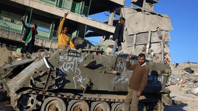 Palestinos posan frente a un tanque israelí destruido en medio de la destrucción que dejaron los ataques militares sobre la Franja de Gaza