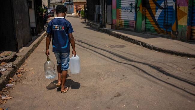 Un hombre en la localidad de Rocinha acarrea botellones con agua en medio de una ola de calor en el estadio de Río de Janeiro en Brasil.